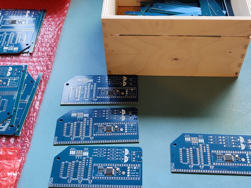 De-panelised PCBs in front of a wooden box with a slot cut in it and half full of PCB offcuts